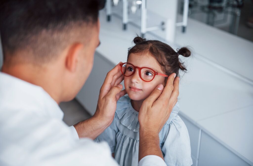 A young child looks at an eye doctor who is helping her to get fitted for a pair of red glasses