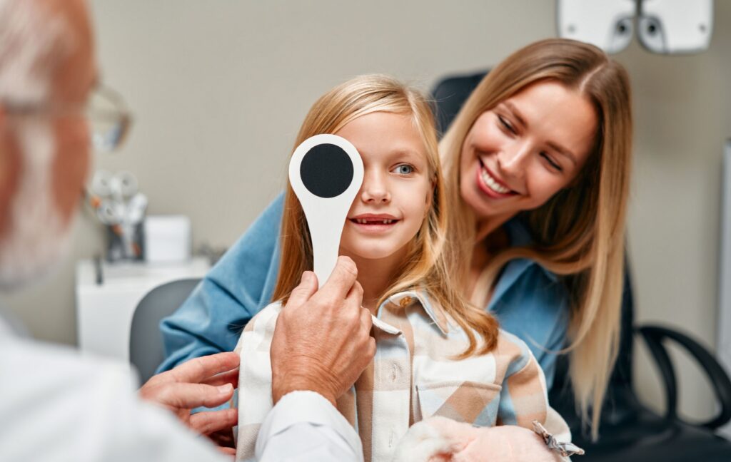 A young child sits in their parent's lap while an optometrist tests the child's vision during an eye exam.