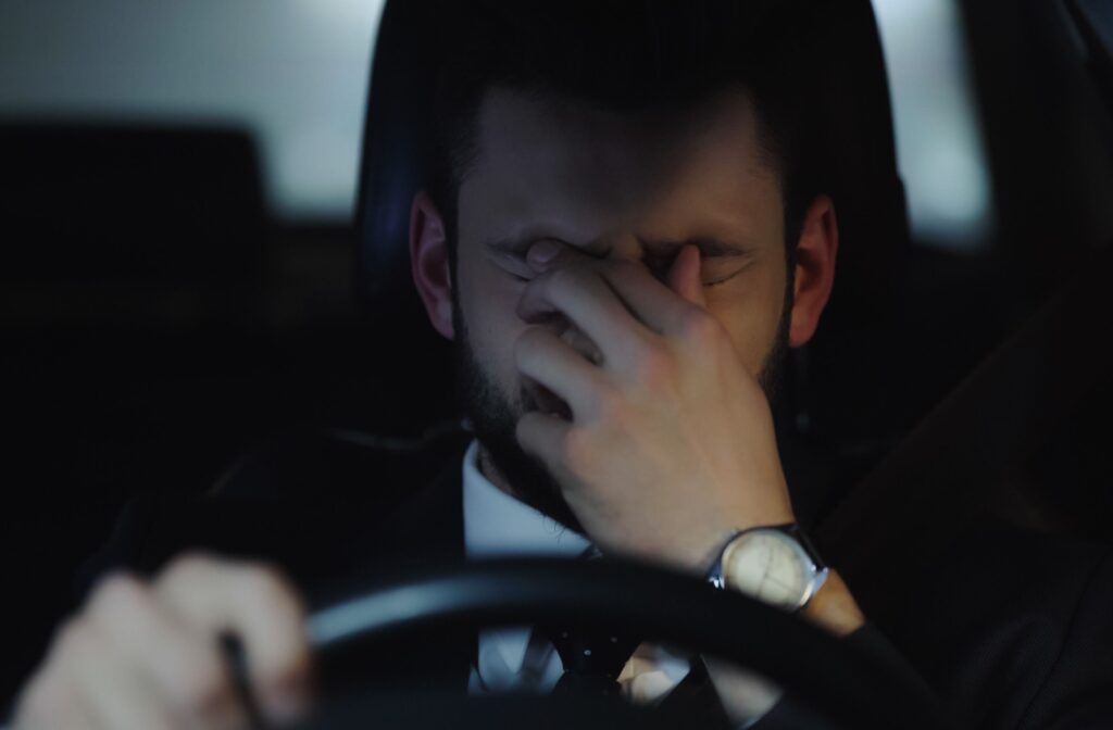 Man sits behind his steering wheel in his car and rubs his eyes with his hand