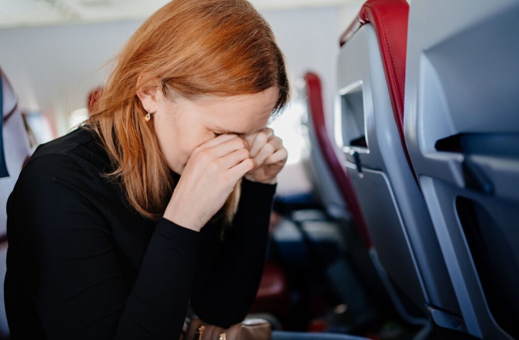 A person experiencing dry eyes while on an airplane rubs their dry eyes