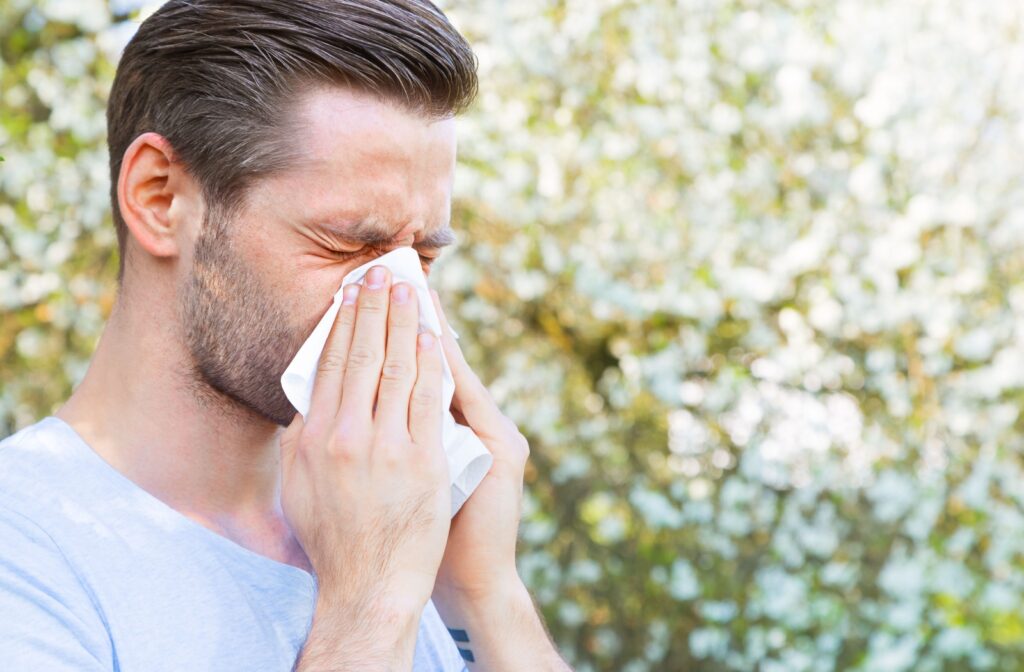 A person blowing their nose due to seasonal allergies while dealing with irritated eyes
